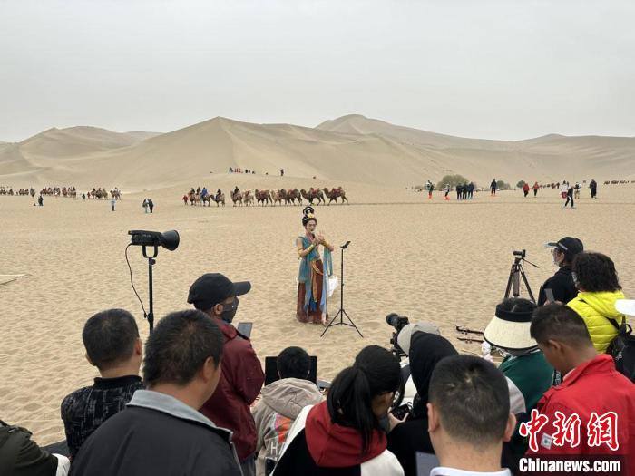 圖為2023年4月底，敦煌大漠“逐舞者”奧楠在鳴沙山月牙泉景區(qū)視頻直播，吸引游人圍觀。　馮志軍 攝